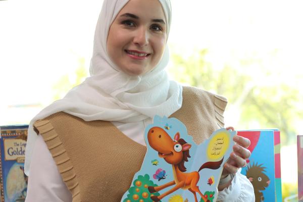 Smiling Arabic woman holding picture book open to page with cartoon horse