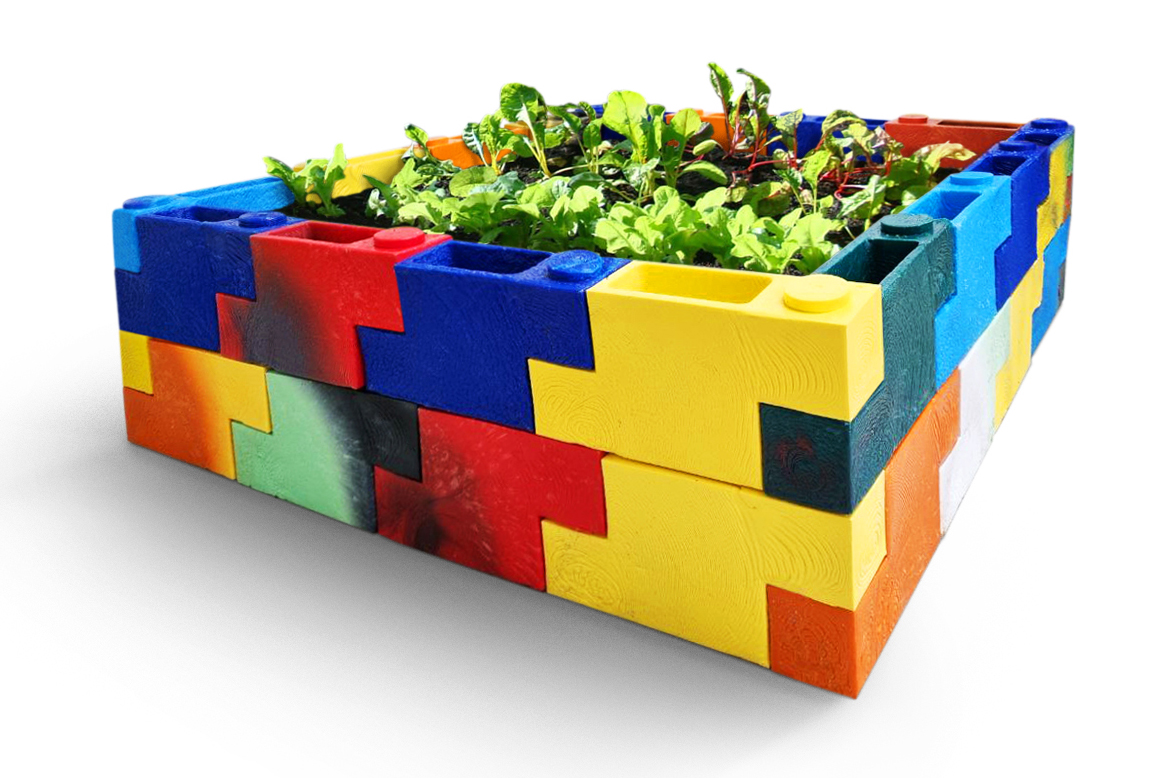 Green leafy vegetables grow from a garden bed made out of colourful lego looking plastic blocks.