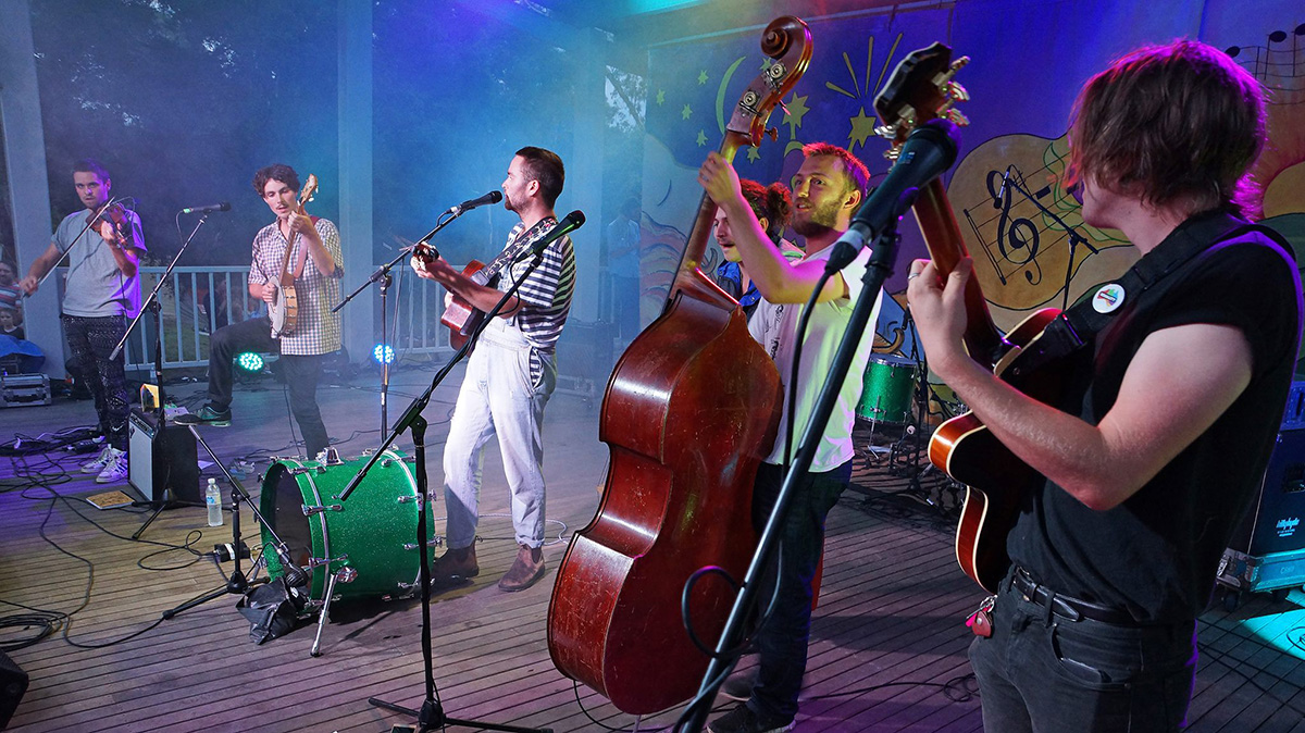 Six members of a string band play music on an outdoor stage