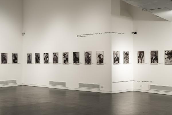 Photograph of the interior of Manningham Art Gallery with 15 photographic portraits on a white wall, with black floor in the foreground