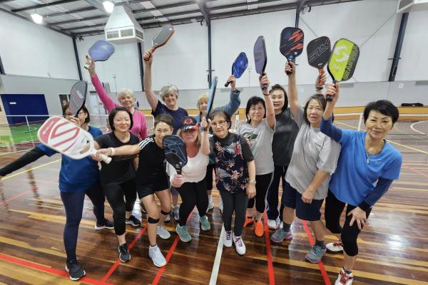 Group of women smiling holding pickleball bats in the air