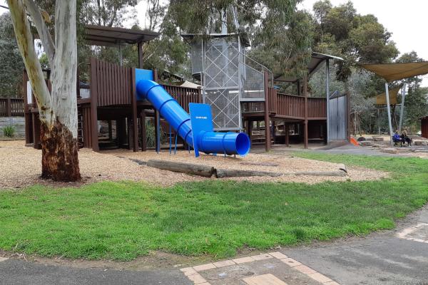 Wooden play structure with enclosed blue slide surrounded by gum trees