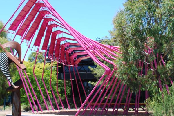 Red metal sculpture in front of a black building surrounded by trees