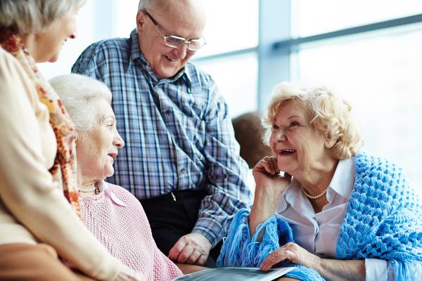 4 elderly people in conversation around armchair laughing