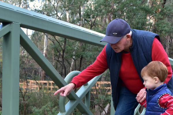 Grandparent and grandchild standing on a bridge looking down at the water below