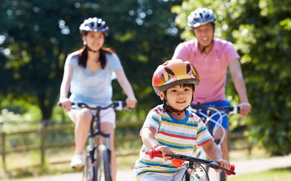 photo of child riding bicycle in front of his parents who are also riding bicycles