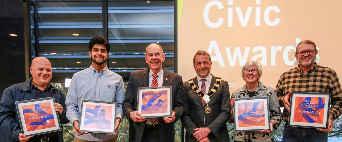 Five civic award winners stand smiling with the mayor, winners are holding their awards in front of themselves
