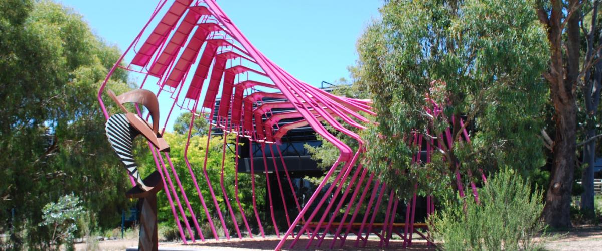 Red metal sculpture in front of a black building surrounded by trees