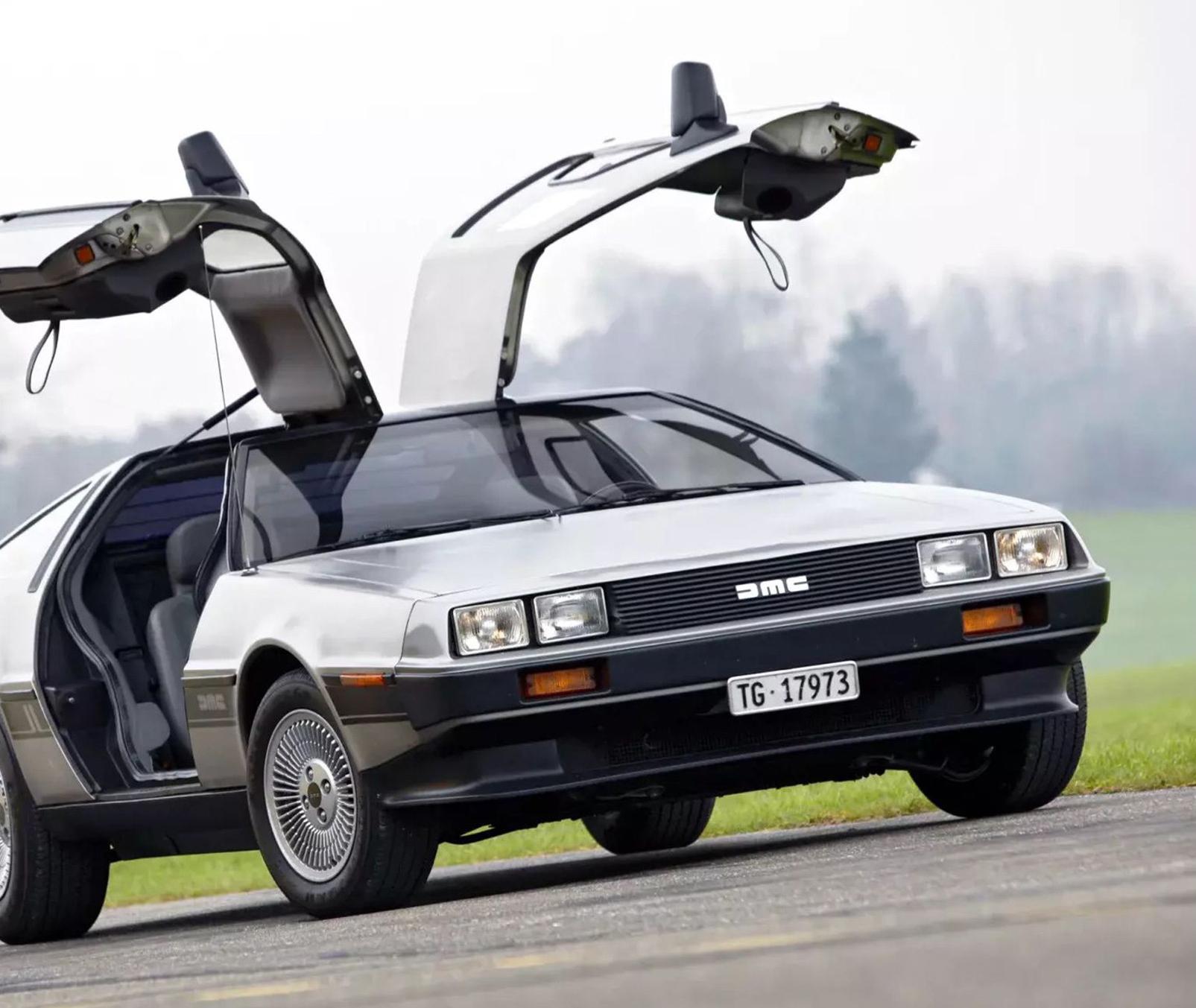 A silver DeLorean with its doors raised up, a misty green forest in the background