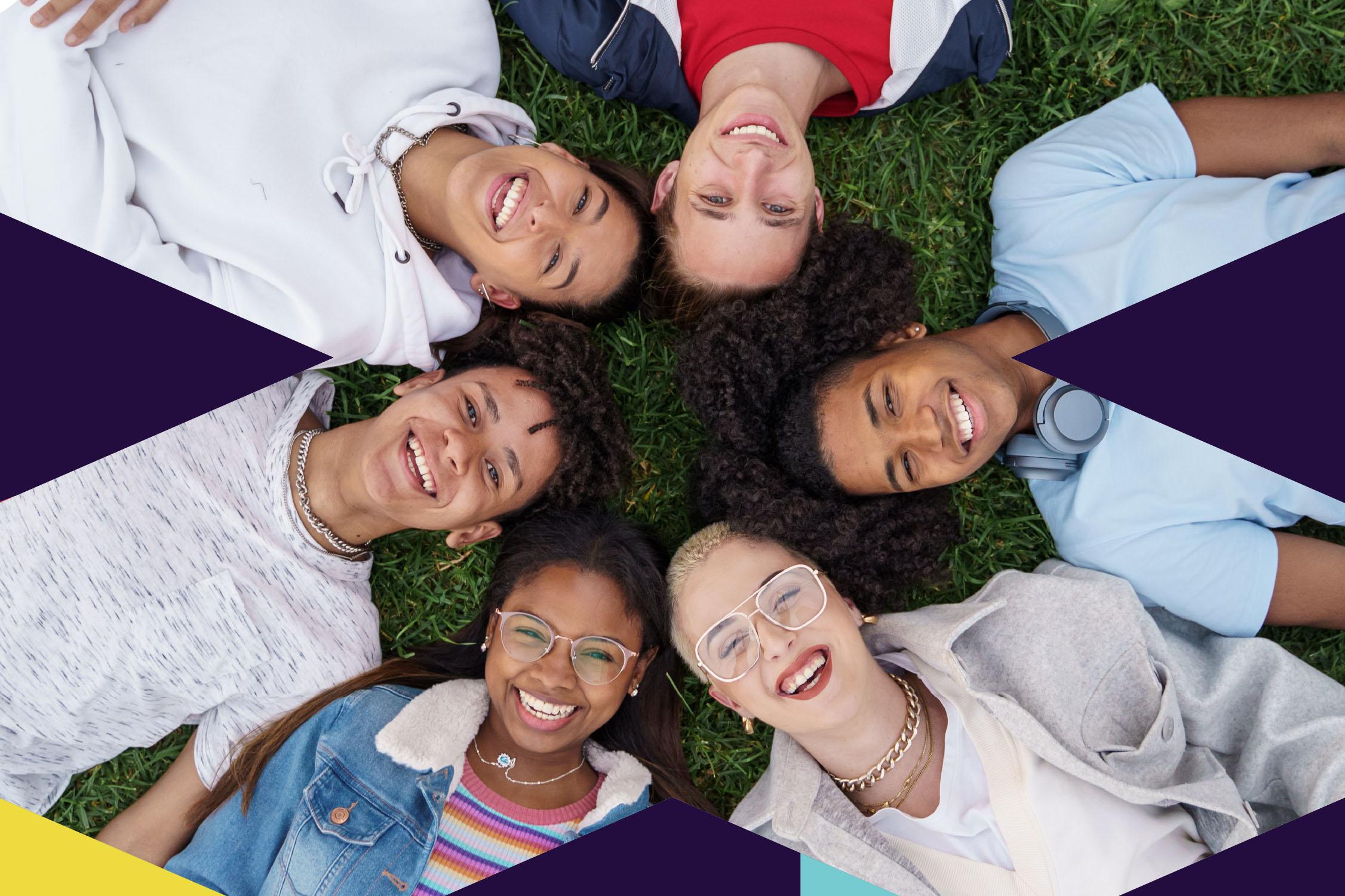 Six young people lay on the ground in a circle with their heads touching, looking up and smiling