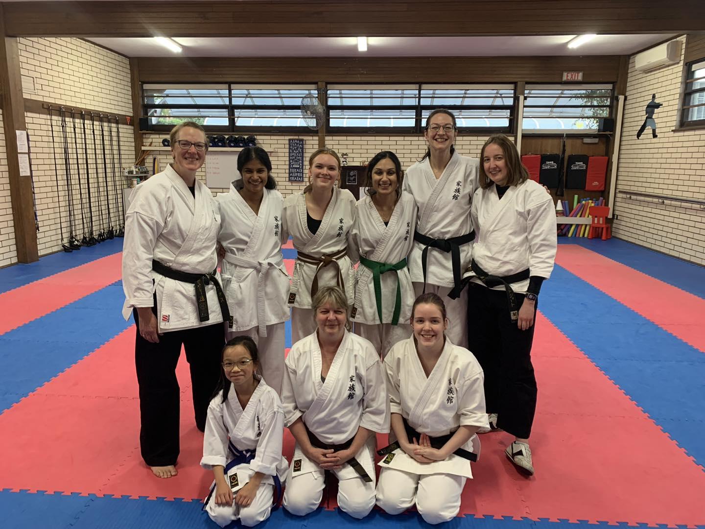 Group of smiling girls and women of different ages wearing karate uniforms in a karate dojo