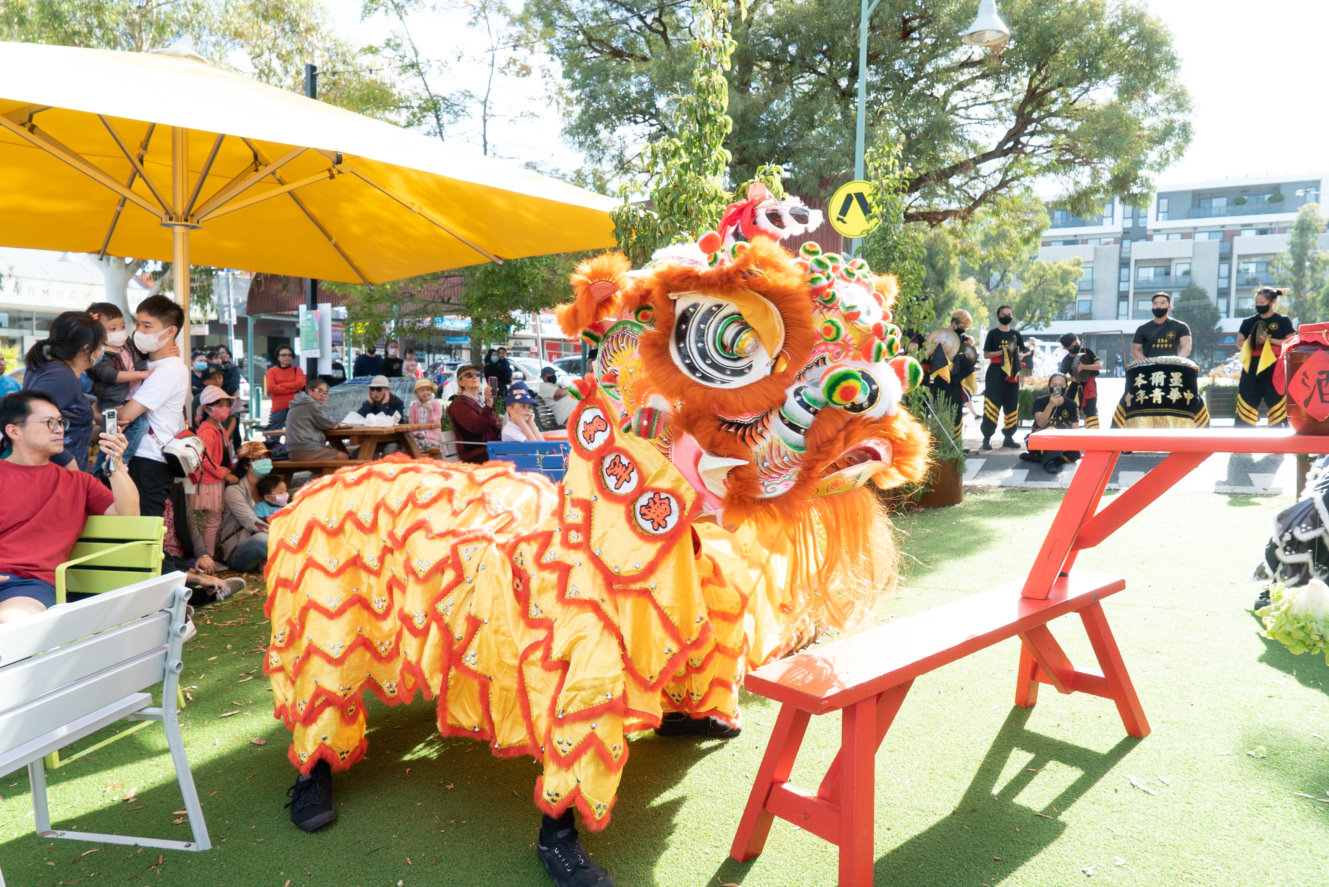 Orange and red Chinese dragon performs for a crowd of onlookers at an outdoor shopping strip
