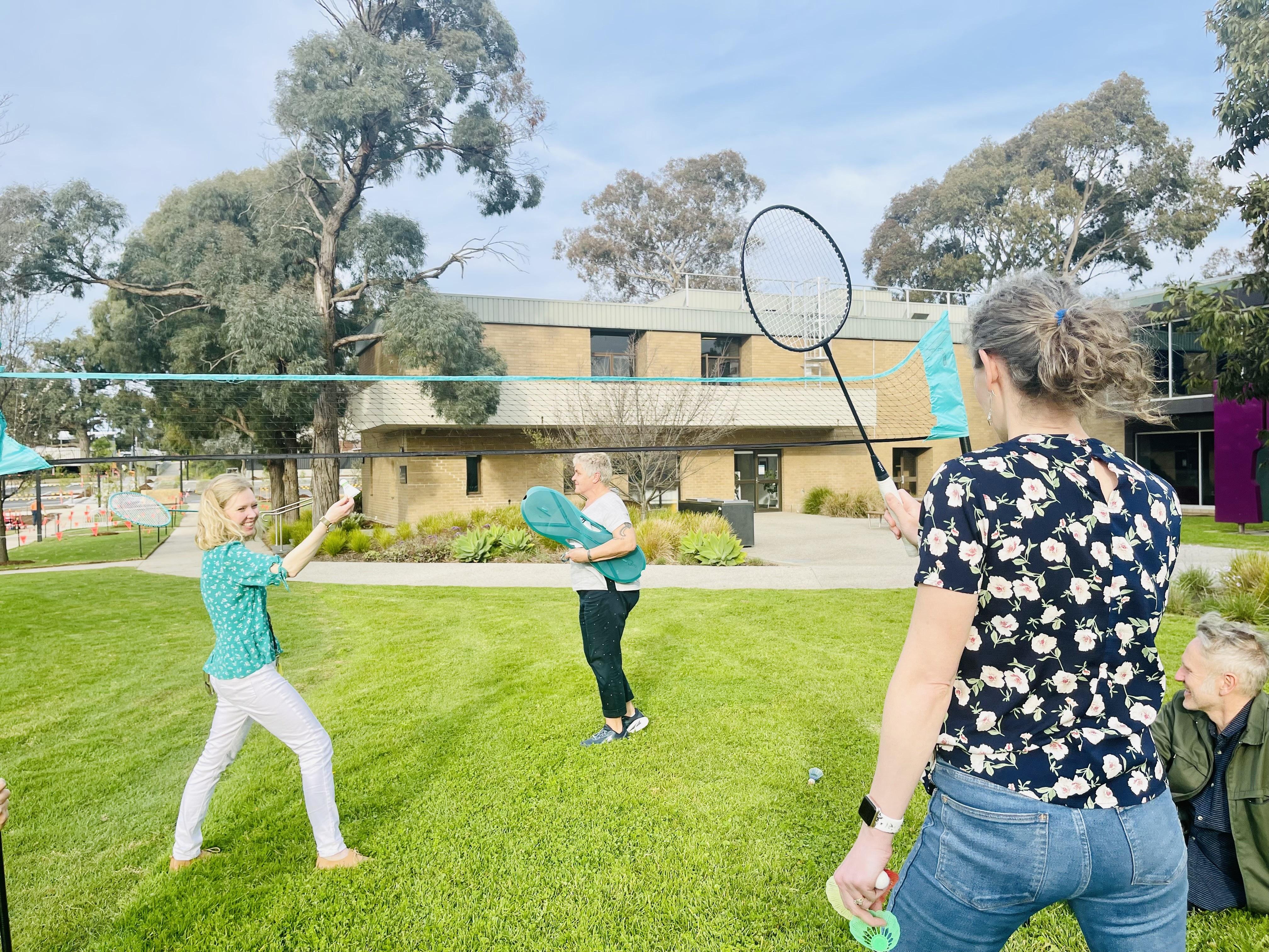4 adults playing outdoor badminton in a park