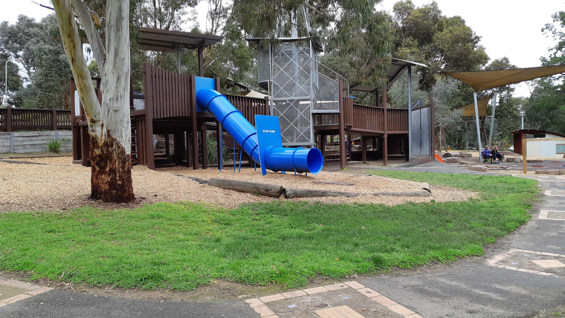 Wooden play structure with enclosed blue slide surrounded by gum trees