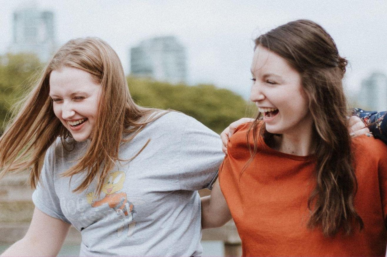 Two young women walk with arms around each other laughing