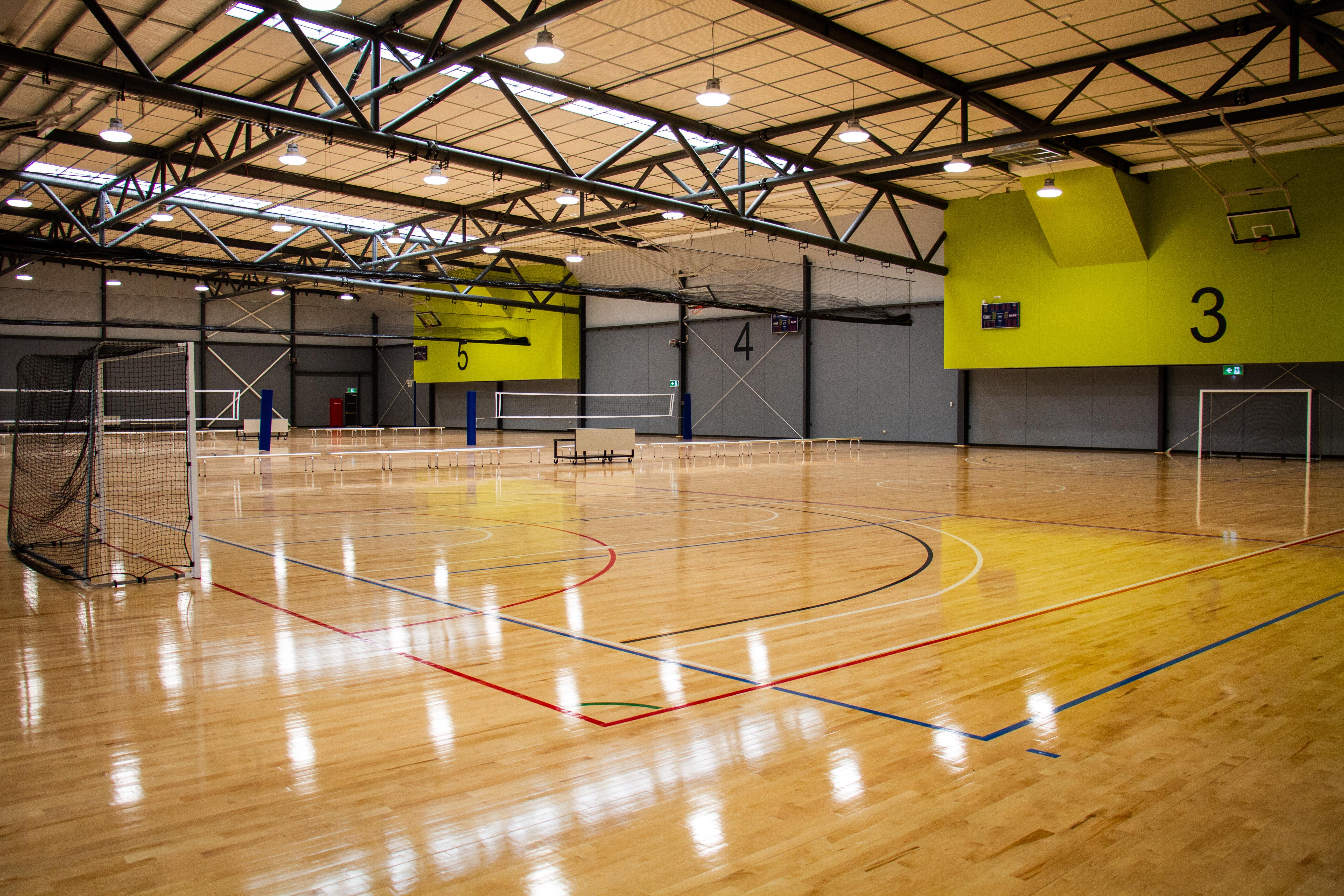 Large indoor multi-sports stadium with soccer goals on court and the numbers 3, 4 and 5 visible on the back wall.