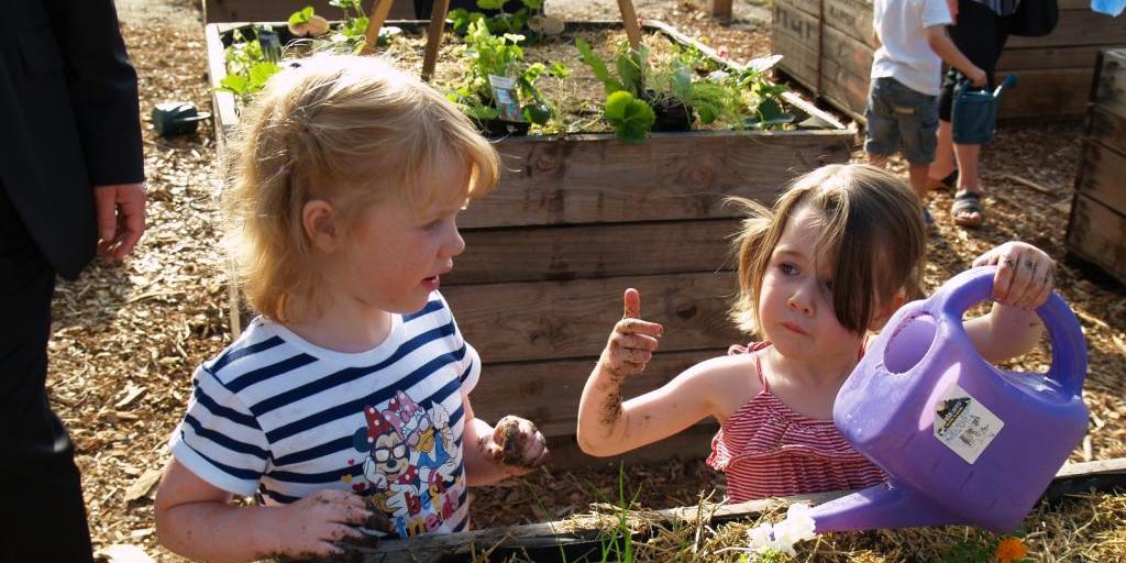 Two young girls at a raised garden bed, one holding a watering can