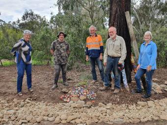 Five people in a bush setting smiling and standing around a colourful pile of rocks