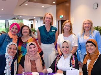 Councillor Deirdre Diamante and attendees at the 2022 International Women’s Day event, which had the theme #BreakTheBias. The women are smiling and sitting and standing around a table with a purple table cloth.