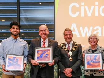 Five civic award winners stand smiling with the mayor, winners are holding their awards in front of themselves