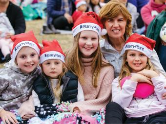 Four girls and one woman smiling together at the Carols wearing Christmas hats