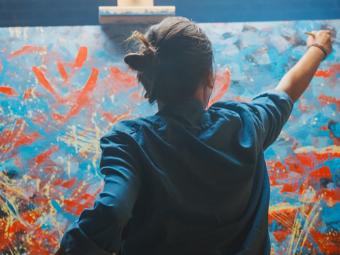 artist painting on large canvas with blue and red paint