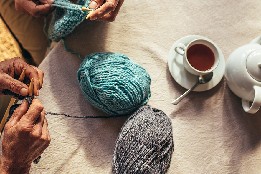 above shot of two hands knitting with a cup of tea