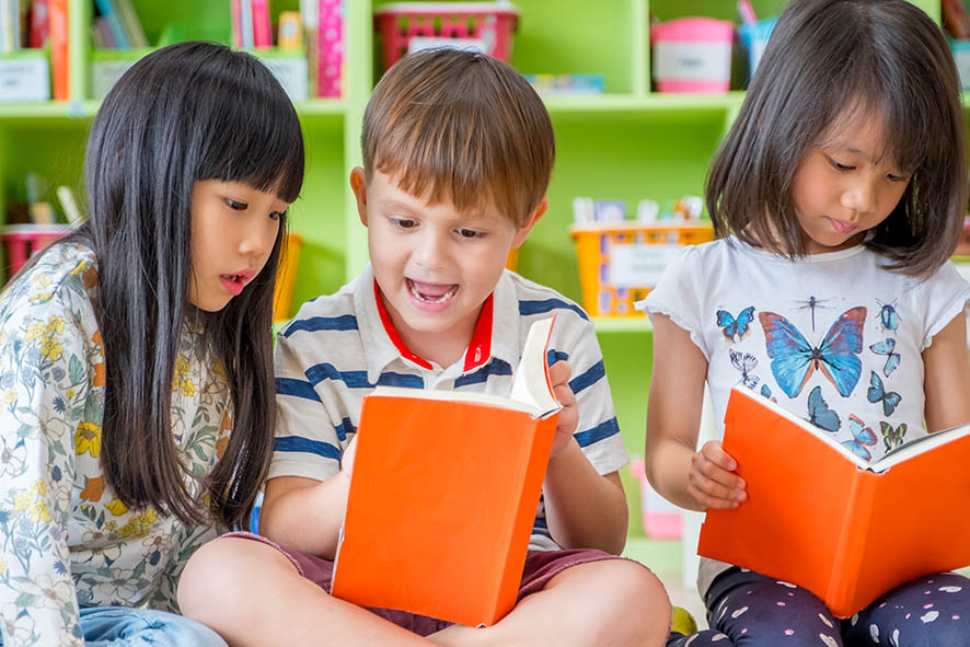 Three children reading books at library
