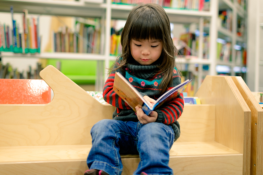 young girl reading book in library