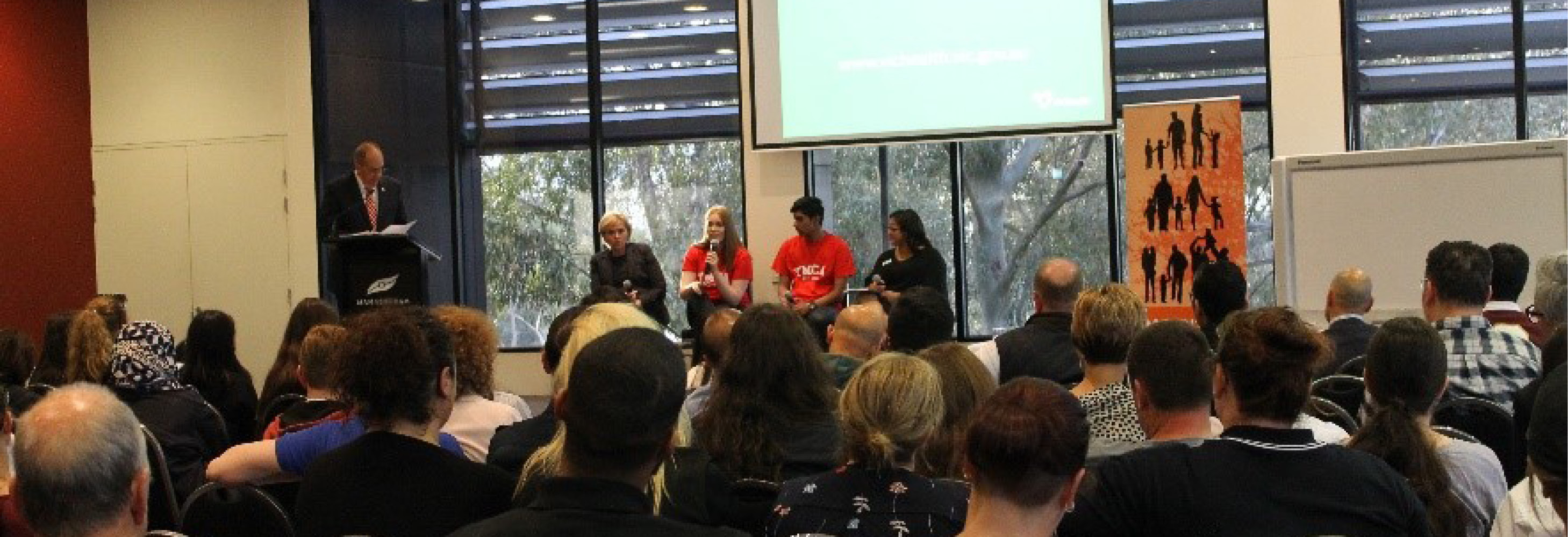 A group of people in a function room listening to a panel of people speak on stage