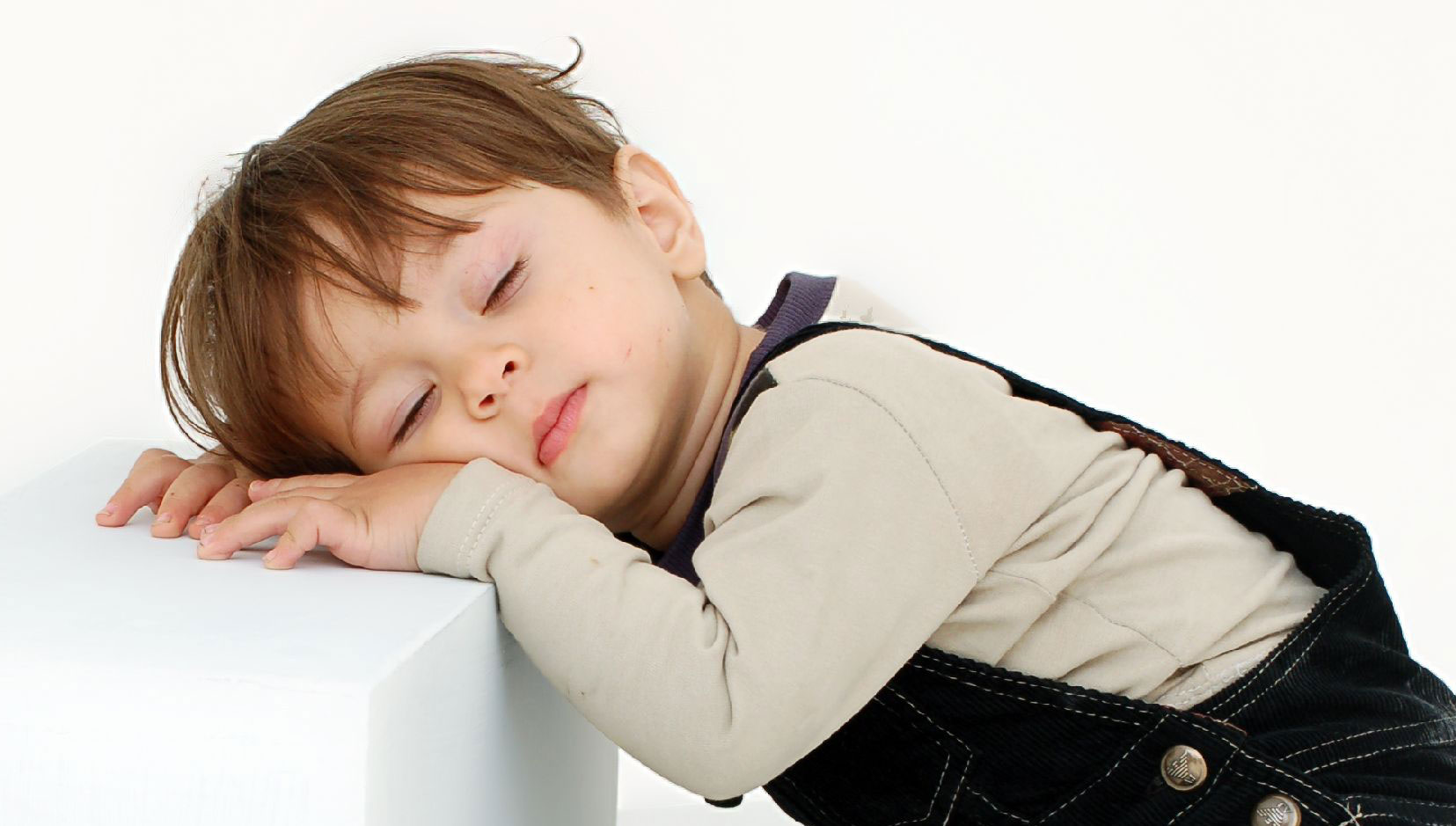 Toddler asleep while standing up with his head resting on a ledge