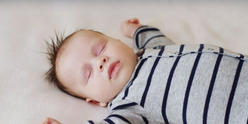 Sleeping baby lying on back with arms up beside their head