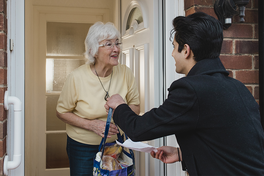 Man delivering an older woman a bag of groceries at the door